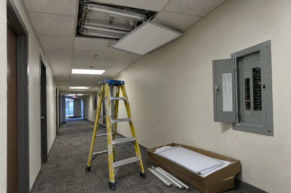 Replacing an old ceiling light fixture with an LED panel in an office hallway